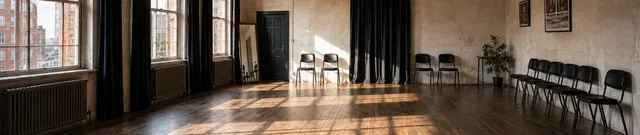 Empty acting studio with a wooden floor, large windows and a row of black chairs